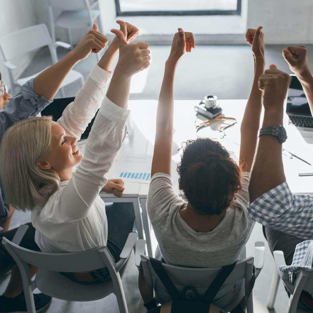 A group of people at a conference table raising their arms in celebration.