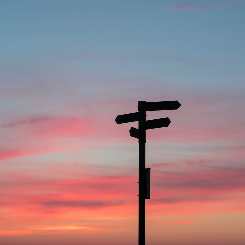 A directional signpost silhouetted against a sunset sky.