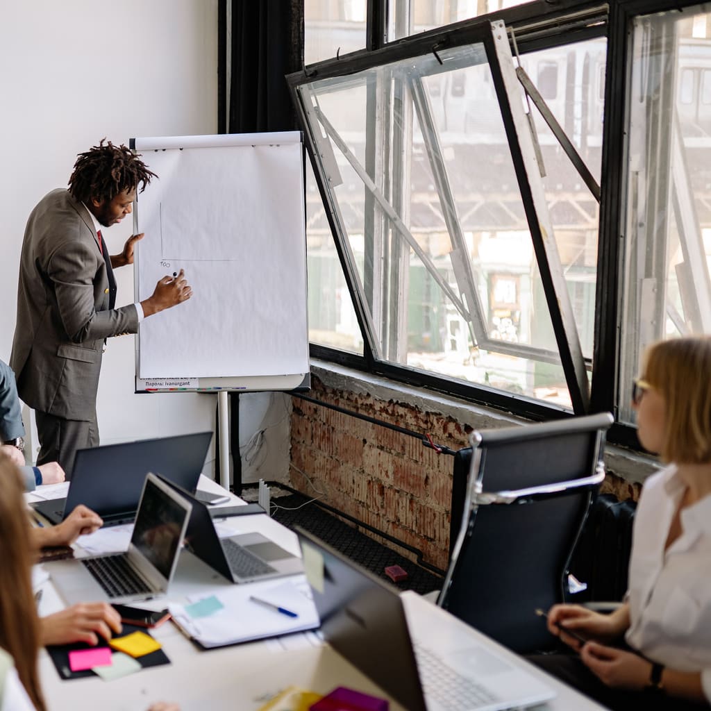 A presenter leads a team workshop at a whiteboard in a bright meeting room.