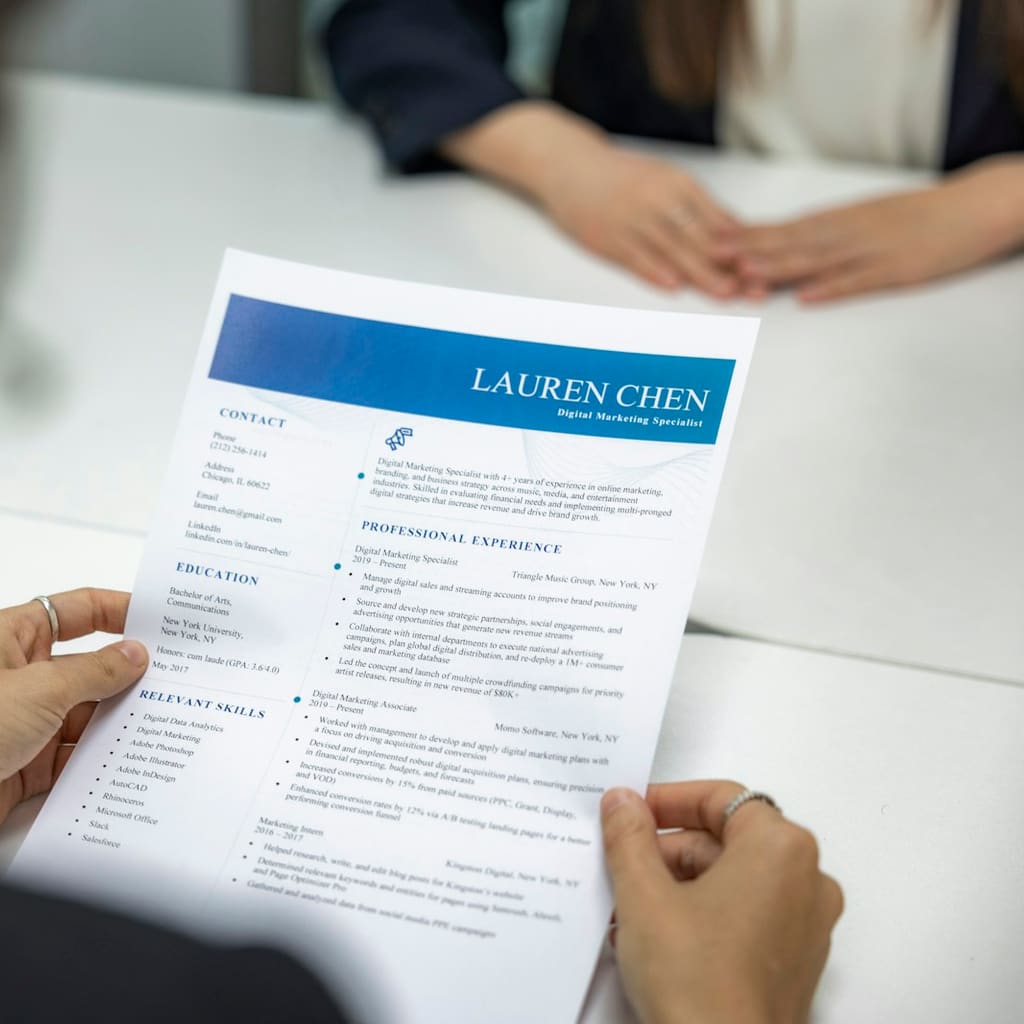 A recruiter holds a printed resume across the table from a candidate.